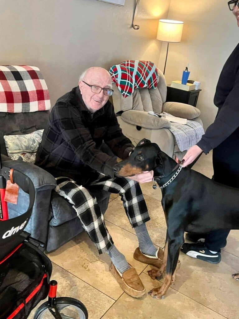 An older man gently pets a dog while sitting comfortably in a chair